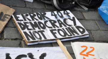 A protest sign laying on the ground reads "Error 404: Democracy Not Found." 