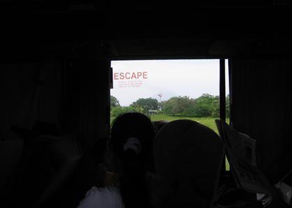 The photo is pretty dark except for a large square in the center, which appears to be a window looking outside to trees and grass. On the left side of the window are is the word "Escape." In the forefront of the picture, one can see the shadow of women looking outside the window.